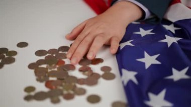 Yakın plan. Beyaz bir masada, katlanmış bir Amerikan bayrağıyla, mavi takım elbiseli bir kadın nikel ve bakır paraları taşıyor.