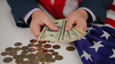 Yakın plan. Tanınmayan bir kadın Amerikan dolarlarını elinde tutuyor, beyaz bir masada, dağınık nikel ve bakır paralardan oluşan bir arka planda oturuyor ve katlanmış bir Amerikan doları...