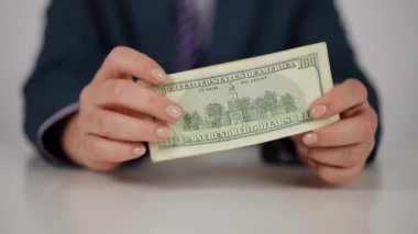 Yakın plan. Ağır çekim. Mavi takım elbiseli tanınmayan bir kadın elinde bir yığın Amerikan doları tutuyor ve beyaz bir masada otururken kameraya doğru sallıyor.