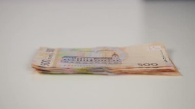 Ağır çekim. Yakın plan. Bir yığın banknotun üzerinde Ukrayna hryvniası beyaz bir masanın üzerinde yatarken, bir kadın eli Amerikan doları ile bir banknot koyuyor.