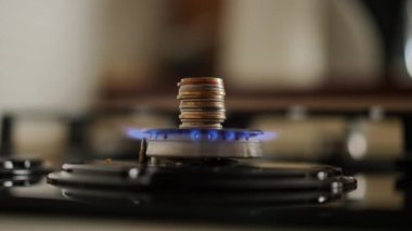 Yakın plan. Gaz ocağının kapağında metal madeni paralar yığını var. Soba yanıyor ve gaz ocağı mavi bir alevle yanıyor.