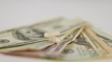 Ağır çekim. Son derece yakın çekim. Beyaz tıbbi kapsüller Amerikan dolarlarının üstüne düşüyor. Beyaz bir masanın üzerindeki pervane gibi.