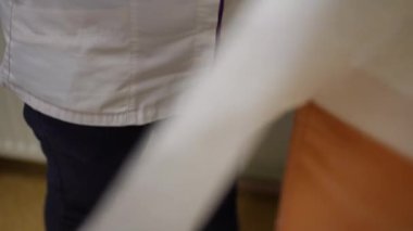 Ağır çekim. Yakın plan. Tanınmayan bir hemşire tek kullanımlık bir bezi açar ve üzerini şehir kliniğindeki bir odanın köşesinde duran tıbbi bir masayla kapatır.