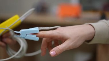 Yakın plan. Adamın biri elinde, içeride sandalyesinde oturan tanınmayan bir kadının parmağına nabız oksimetresi sensörü takıyor. Doktor hastaya oksijen doygunluğunu ölçer.