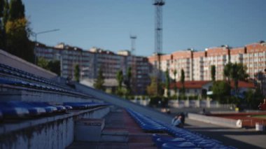 Ağır çekim. Şık erkek sporcu hızla koşuyor, stadyumun merdivenlerinden atlıyor. Güneş gözlüklü ve rastalı bir adam sıcak bir sonbahar gününde dışarıda antrenman yapıyor.