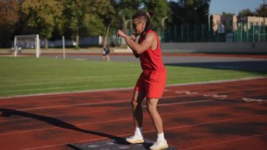 Güneş gözlüklü ve rastalı şık bir sporcu boks yapıyor, sonbahar günü stadyumun koşu pistinde uzanan spor minderinde daireler çiziyor.