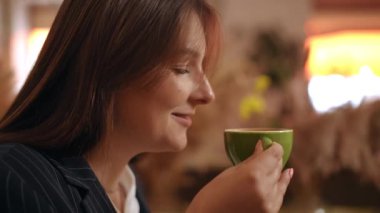 Yakın plan. Bir kadın, kafedeki bir masada otururken yeşil bir porselen fincanda kahve kokusunun tadını çıkarır.