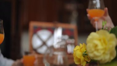 Yakın plan. Arkadaşlar şenlik masasında otururken şarap kadehlerini portakal suyuyla tokuştururlar.