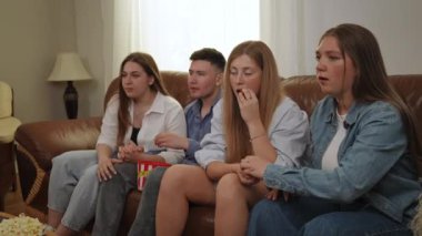 Bir futbol maçını izlerken arkadaşlarla duygusal anlar. Oturma odasındaki deri koltukta oturan arkadaşlar büyük plastik bir bardaktan patlamış mısır yiyip duygusal tepki veriyorlar.