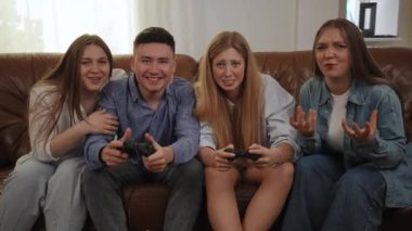 Arkadaşlarla birlikte bir konsolun üzerinde deri koltukta oturan bir video oyunu. Elinde av sahası olan neşeli bir adam online bir oyunda yanında oturan bir kızdan kazanıyor.