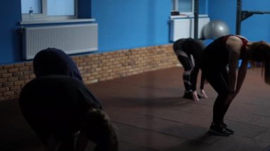 Ağır çekim. Kadınlar spor salonunda kapalı yerde dururken spor yaparlar. Spor giyimli bir grup kadın yavaşça ayağa kalkar.