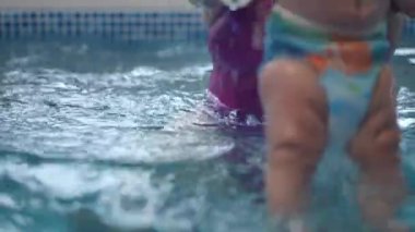 Yakın plan. Tanınmayan bir kadın, en uygun su sıcaklığına sahip bebekler için bir yüzme havuzunda bebeği suya alıştırıyor.