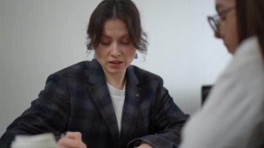 Yakın plan. Spor ceketli bir kadın yönetici, genç bir çalışana sorunun özünü anlatıyor. Masada yatan tabloya işaret ediyor. Bir iş kadını kağıt bardaktan kahve içiyor ve...