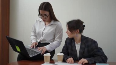 Gözlüklü bir kız kucağında dizüstü bilgisayarla masanın üstünde oturuyor ve masada oturan bir iş arkadaşını bulmak için internette bilgi arıyor. Masada dosyalar ve iki tane var.