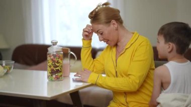 Bir kadın oturma odasındaki masada otururken cep telefonu kullanıyor. Küçük bir çocuk annesine yaklaşıyor, dikkatleri üzerine çekiyor. Anne gülümser ve çocuğuna sarılır.