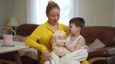 Genç bir oğul annesinin kucağına oturur ve elinde tuttuğu oyuncak ayıyla oynar. Anne ve oğlu sabahın erken saatlerinde oturma odasındaki masada oynuyorlar.