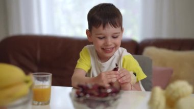 Oyuncak ayıyla gülümseyen küçük bir çocuk, oturma odasındaki bir masada bir sandalyede otururken elinde bir şekeri açıyor. Anne küçük çocuğa doğru yürür ve o gülerek şekeri saklar.