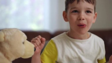 Yakın plan. Neşeli küçük bir çocuk masadaki makarnayı dudaklarıyla alıyor ve gülümseyip kameraya poz vererek yiyor.