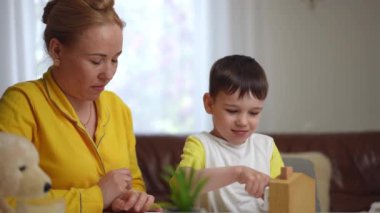 Bir anne, modern bir evin oturma odasındaki bir masada otururken oğlunun tahta bir takvim evinden küp çıkarmasını izler. Küçük bir çocuk ahşap sayı küpüne dikkatle bakar.