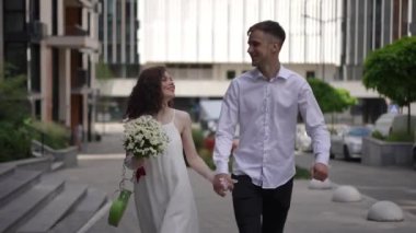 Güneşli bir yaz gününde, mutlu, gülümseyen bir çift şehir bloğunun kaldırımında yürüyor. Kız bir elinde papatya buketi, diğerinde de oğlanlarla el ele tutuşuyor.