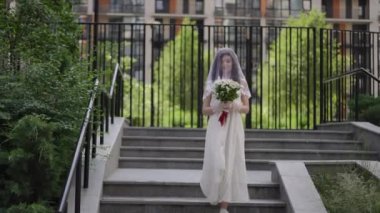 Yüzünde duvak olan gelinlik giymiş bir kız bir yaz günü şehir merdiveninin granit basamaklarından iniyor. Gelin elinde kırmızı kurdeleyle bağlanmış bir buket beyaz papatya tutuyor.