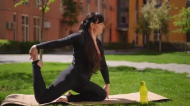 Eşofmanlı bir kadın yoga yaparken yoga yapıyor. Bir bahar günü, bir apartmanın bahçesinde yoga minderinin üzerinde diz çökerken.