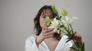 Beyaz zambaklarla süslenmiş bir kadının büyüleyici portresi sükuneti ve nefis güzelliği çağrıştırıyor.