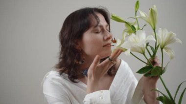 Huzurlu ve huzurlu bir kadın, her an zarafet ve güzelliği somutlaştıran güzel beyaz zambaklarla nazikçe etkileşir.