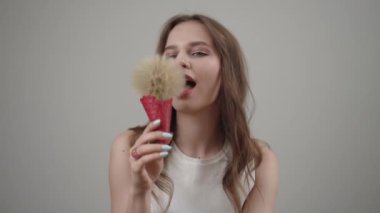 Genç bir kadın, basit ve sade bir arkaplan önünde yumuşak bir fırçayla poz vererek güzelliğini sergiliyor.