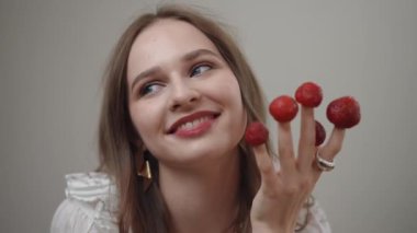 Şık ve kendine güvenen genç bir kadın elinde taze ve sulu ahududular tutuyor. Eğlenceli ve modaya uygun bir hava sergiliyor.