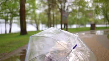 Parlak yağmurluklu neşeli bir kız, yemyeşil bir yolda açık bir şemsiye tutuyor.