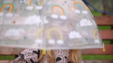 Yağmurlu bir günde şeffaf bir şemsiye tutan genç bir kız neşeli ruhunu mükemmel bir şekilde sergiliyor.