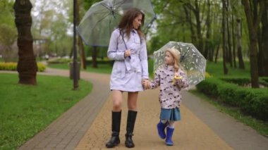 Yağmurlu bir günde yemyeşil bir parkta renkli şemsiyeler tutan bir anne ve kızın yürek ısıtan anı.