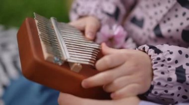 Neşeli bir çocuk, mutlu bir şekilde renkli çiçeklerle çevrili bir kalimba çalıyor, doğadaki huzurlu bir anı yakalıyor.