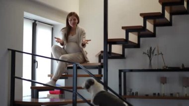 Rahat bir merdivende oturan, modern ev estetiğini güzelce sergileyen hamile bir kadının sakin bir sahnesi.