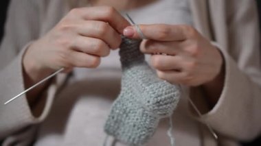 Yumuşak gri bir çorabı ustalıkla ören, el sanatlarının güzel sanatını ön plana çıkaran ellerin detaylı bir yakın çekimi.