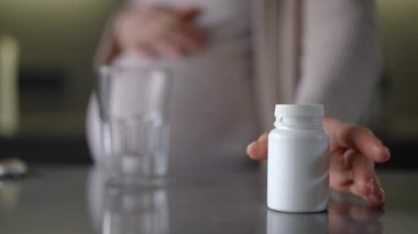 Beyaz ilaç şişesinin detaylı yakın plan görüntüsü, genel sağlık ve ilaç tedavisini sembolize eden bir bardak eşliğinde.