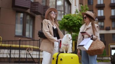 İki şık giyimli kadın, yanında bir köpek ve bavullarıyla şehirde harika bir gün geçiriyorlar.