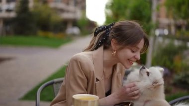 Tarz sahibi bir kadın, güzel yeşil bir alanda kahvesini yudumlarken tüylü köpeğiyle etkileşime girer ve neşe yaratır.