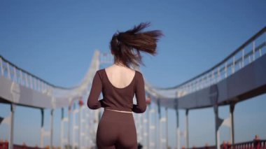 Bir kadın koşucu güneşli bir günde büyüleyici ve eşsiz bir mimari köprü boyunca keyifle koşar.
