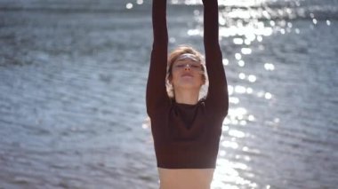 Huzurlu ve huzurlu bir an. Bir kadın zarif bir şekilde yoga yapıyor. Işıl ışıl ve güzel bir suyun yanında.