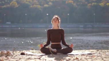 Huzurlu ve huzurlu bir sahne, güzel sonbahar titreşimleriyle çevrili, suyun kenarında huzur içinde meditasyon yapan bir kadını gösteriyor.