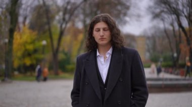 Düşünceli bir birey, canlı sonbahar ağaçları ve yapraklarıyla çevrili sakin bir parkta huzur içinde duruyor.