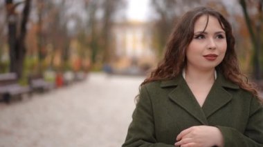 Zarif ve zarif bir kadın zarif bir sonbahar parkı ortamında duruyor, canlı yapraklarla çevrili.