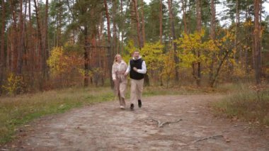 Ağır çekim. Sevgi dolu bir çift, güzel bir sonbahar ormanı yolunda el ele romantik bir gezintiden zevk alır.