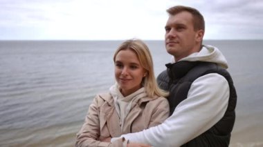 Sevgi dolu bir çift, bulutlu bir gökyüzünün altındaki sakin ve davetkar okyanusta sıcak ve samimi bir kucaklaşmayı paylaşır.