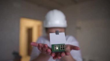 Bir inşaat işçisi, gayrimenkul ve konut gelişimini sembolize eden minyatür bir ev modeli sergiliyor..
