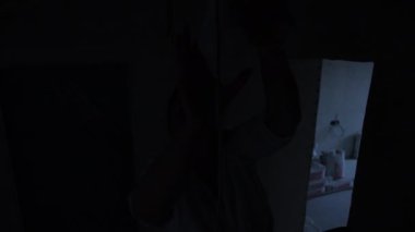 Loş bir alanda gizemli bir figür var. Ampulü prize sokuyor..