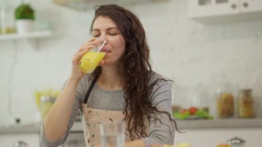 Bir kadın şık bir mutfakta taze meyve suyunun tadını çıkarıyor, sağlıklı yaşam tarzını ve yemek zevkini sergiliyor..