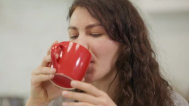 Düşünceli bir kadın bu rahat ve rahat atmosferde kırmızı bardağını yudumlayarak sıcak bir içkinin tadını çıkarıyor.